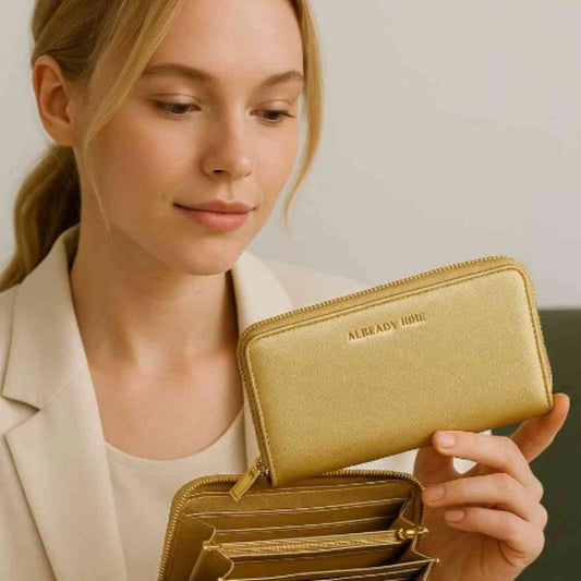 A stylish woman holding a gold zip-around wallet with "ALREADY MINE" embossed on it, showcasing the wallet as a Feng Shui accessory for attracting wealth and abundance in 2025.